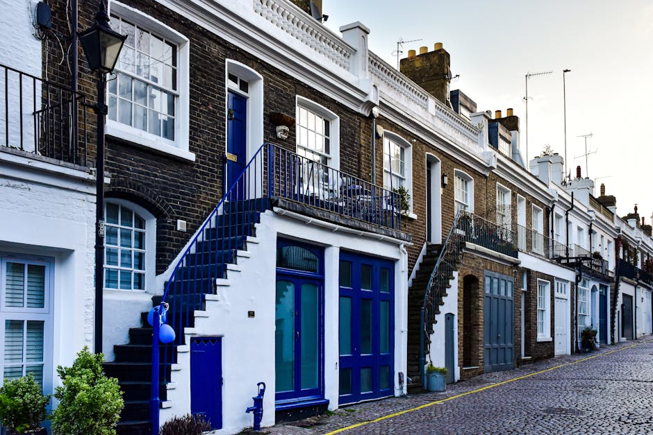 A row of white residential terraced houses with bay windows and decorative moldings, situated along a tree-lined street in Putney. The street features parked cars including a grey Audi and a black Min